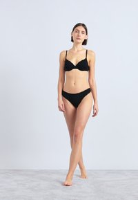 Mustast pesukomplektidest koosnev komplekt, kus on polsterdatud rinnahoidja ja sobivad bikini-stiilis aluspüksid, peene pitsiäärise ja reguleeritavate rihmadega.
