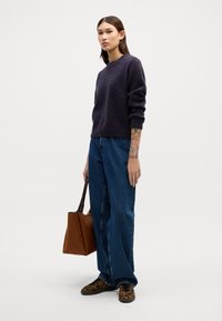 Dunkelviolett, strukturierter Strickpullover; lockere, hochgeschnittene blaue Jeans; Sneakers mit Leopardenmuster; braune Tote-Tasche. Einfaches, lässiges Outfit.