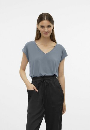 T-shirt blu con scollo a V e maniche corte, indossato con pantaloni neri con coulisse e tasche laterali, esposto su uno sfondo semplice.