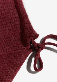 Burgundi värvi kudum, millel on tekstuuriga pind ja sidepinna detail servas kindlaks kinnitusks.