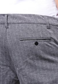 Pantalones gris a rayas con una textura suave, con un solo bolsillo trasero con cierre de botón negro. Diseño de cintura estándar.