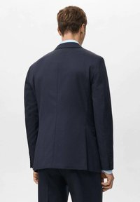 Giacca da abito blu navy con una consistenza liscia, spacco singolo sul retro, rever a lancia e dettagli con polsini a tre bottoni.