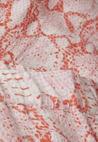Tessuto leggero con un motivo astratto rosa e arancione, caratterizzato da una superficie texturizzata e dettagli arricciati sulle cuciture.