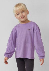 Paarse lange mouw shirt van zacht materiaal, voorzien van puffed sleeves en drie donkerbruine bloemiconen op de voorkant. In combinatie met donkere leggings.