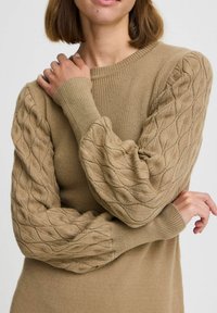 Stickad tröja i beige med ribbat framstycke och texturerade, kabelstickade ballongärmar. Har rund halsringning och åtsittande manschetter.