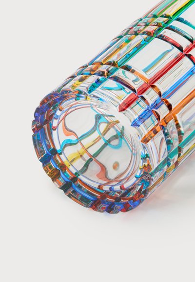 Gros plan d'un objet cylindrique transparent avec des motifs géométriques colorés et des reflets sur fond blanc.