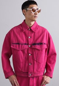 Jachetă din denim fucsia cu două buzunare frontale, nasturi argintii și guler. Textură netedă, croială lejeră și set asortat de pantaloni.