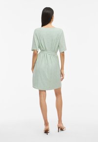 Mintgrön klänning med korta ärmar, texturerat mönster, avslappnad passform och ett matchande bälte i midjan. Slät tyg, längd över knäna.