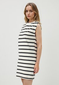 Gestreepte jurk met een ronde halslijn, mouwloos ontwerp, gemaakt van zachte stof met zwarte strepen op een witte achtergrond.