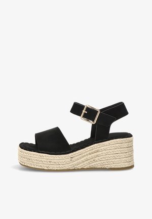Sandalia de cuña de ante negro con suela plataforma gruesa de yute trenzado y correa de hebilla dorada en el tobillo, vista lateral sobre fondo blanco.