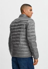 Grijze pufferjack met een gequilte uitstraling, hoge kraag en een soepele textuur, gekenmerkt door horizontale stiksels en een slim fit.