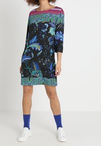 Svart klänning med trekvartslånga ärmar, med färgglada blommönster och abstrakta mönster, rund halsringning och en enfärgad nederkant.