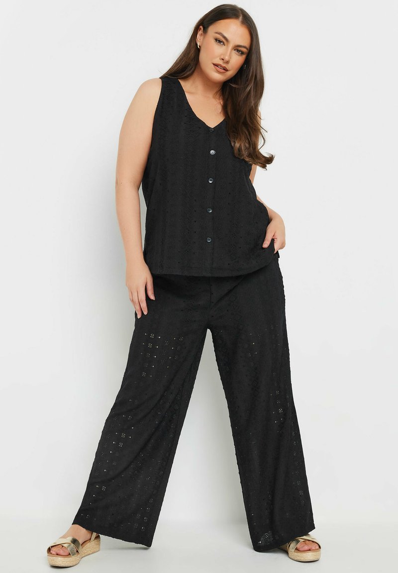 Top senza maniche nero con scollo a V e chiusura a bottoni, abbinato a pantaloni ampi con un design testurizzato a fori.