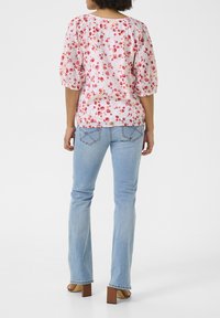Blusa floreale con motivi rosa e rossi, maniche a palloncino e scollatura rotonda, abbinata a jeans azzurri svasati e sandali con tacco squadrato marroni.