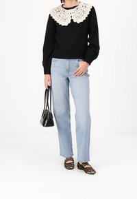 Pull noir avec un col en dentelle blanche, jean bleu clair à jambe droite, et sac à main noir. Ballerines marron à imprimé animal avec des lanières croisées.