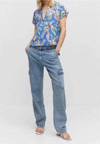 Blusa floreale a maniche corte nei toni del blu, verde e rosa, abbinata a pantaloni cargo leggeri di colore blu chiaro, con tasche laterali.