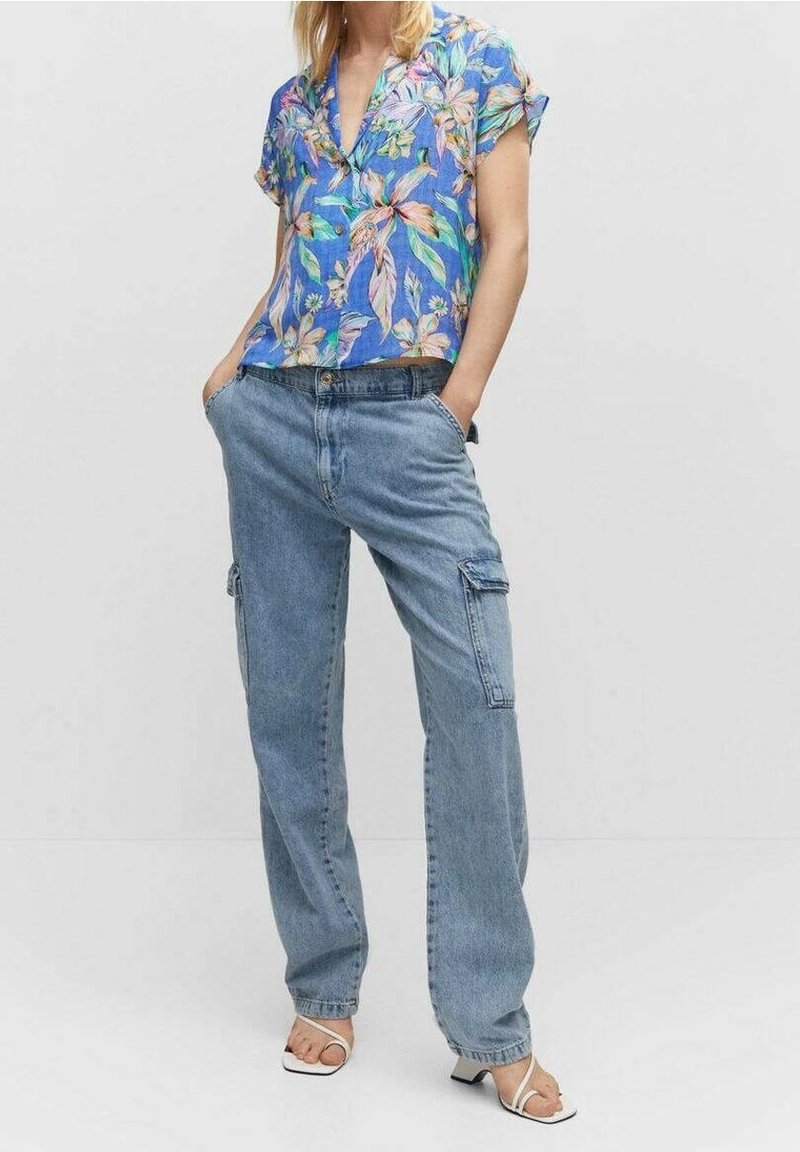Blusa floreale a maniche corte nei toni del blu, verde e rosa, abbinata a pantaloni cargo leggeri di colore blu chiaro, con tasche laterali.
