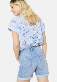 Light blue short-sleeve shirt with eyelet floral designs, paired with light denim shorts featuring rolled cuffs and back pockets.