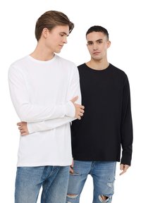 T-shirt a maniche lunghe in bianco e nero, realizzata con un tessuto morbido, con scollatura a girocollo e polsini aderenti, abbinata a jeans blu strappati.