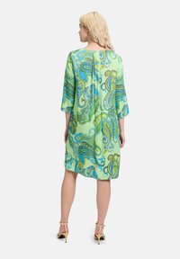 Groene jurk met paisleypatroon, driekwartmouwen en een losse fit, voorzien van een rugplooien en een zachte stofstructuur, gecombineerd met haksandalen.