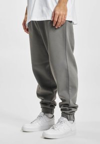 Pantalones deportivos de mezcla de algodón gris con puños elásticos, bolsillos laterales y un ajuste relajado, combinados con zapatillas deportivas blancas.