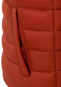 Nahaufnahme einer roten gesteppte Jacke, die eine teilweise offene seitliche Reißverschlusstasche zeigt, mit passendem roten Reißverschlussanhänger.