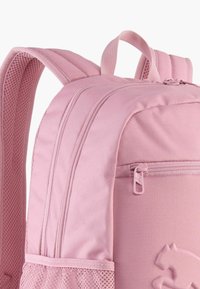 Mochila rosa con tejido suave, correas acolchadas, un bolsillo delantero con cremallera y un bolsillo lateral de malla. Incluye detalle del logo en el cuerpo.