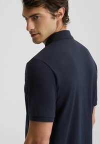 Polo in navy con tessuto testurizzato, maniche corte e colletto classico. Il modello è mostrato di spalle, evidenziando la vestibilità e la struttura.
