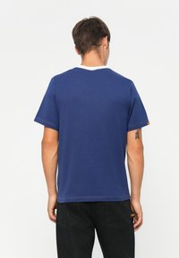 Kortærmet blå t-shirt med rund hals, kontrasterende hvid krave og subtile syninger. Etiketten synlig på venstre ærme.