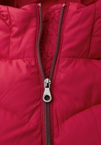 Veste rouge matelassée avec une fermeture éclair en métal argenté partiellement dézippée au centre devant, montrant des détails de couture matelassée.