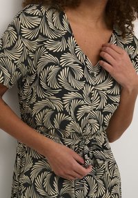 Schwarzes Kleid mit V-Ausschnitt, kurzen Ärmeln und tailliertem Gürtel. Der Stoff zeigt ein cremefarbenes Blättermuster und hat eine Knopfleiste an der Vorderseite.