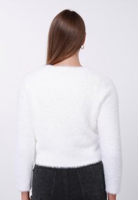 Λευκό, αφράτο πουλόβερ με στρογγυλή λαιμόκοψη και μακριά μανίκια, με απαλή υφή. Συνδυασμένο με σκούρο γκρι παντελόνι ψηλόμεσο.