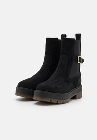 Czarne zamszowe botki za kostkę z okrągłym noskiem, grubą platformą, elastycznymi bocznymi panelami i akcentem w postaci klamry na obcasie.