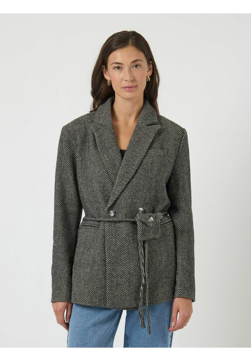 Grijs-zwart blazer met visgraatmotief, een sjaalkraag, een tailleband en twee knopen. Heeft lange, gestructureerde mouwen en zijzakken.