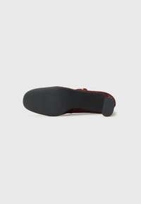 Tacco in suede bordeaux con suola in gomma nera texture e piccolo copritacco. Presenta un design minimalista e una superficie superiore liscia.