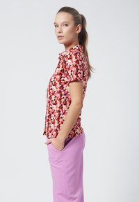 Floral short-sleeve shirt with a red, pink, and white pattern; lightweight fabric; paired with purple trousers featuring side pockets.