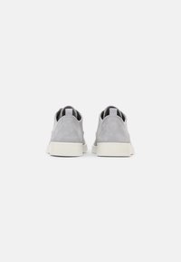 Sneaker in suede grigio con design a collo basso, suole in gomma bianca e linguette posteriori. Texture liscia, stile minimalista e area del tallone rinforzata.