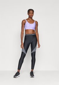 Sujeción deportiva morado con tirantes finos, combinada con unas mallas negras y grises con un diseño geométrico. Ambas están hechas de un tejido elástico y que absorbe la humedad.