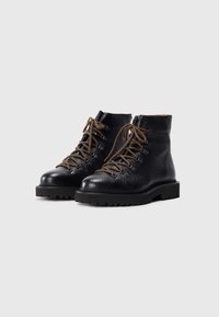 Schwarze Lederstiefeletten mit einer strukturierten Oberfläche, braunen Schnürsenkeln und einer massiven schwarzen Sohle mit robustem Profil.