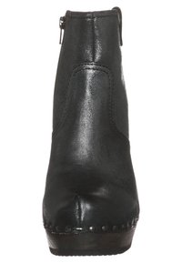 Botín negro de cuero hasta el tobillo con textura suave, punta redondeada, cremallera trasera y tachuelas decorativas a lo largo de la suela.