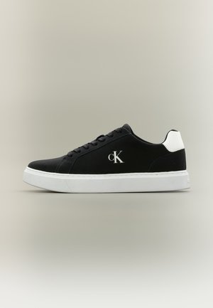 Baskets basses noires avec semelle blanche et languette au talon, lacées à l'avant et logo "cK" sur le côté.