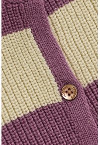 Close-up van paars en crème ribbeltricot met een ronde koperen knop waarop "nopples" is gegraveerd.