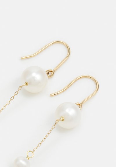 Korvakorut kultasävyssä, joissa on suuria valkoisia helmiä ripustettuna hienovaraisille ketjuille, korostaen tyylikästä ja minimalistista muotoilua.
