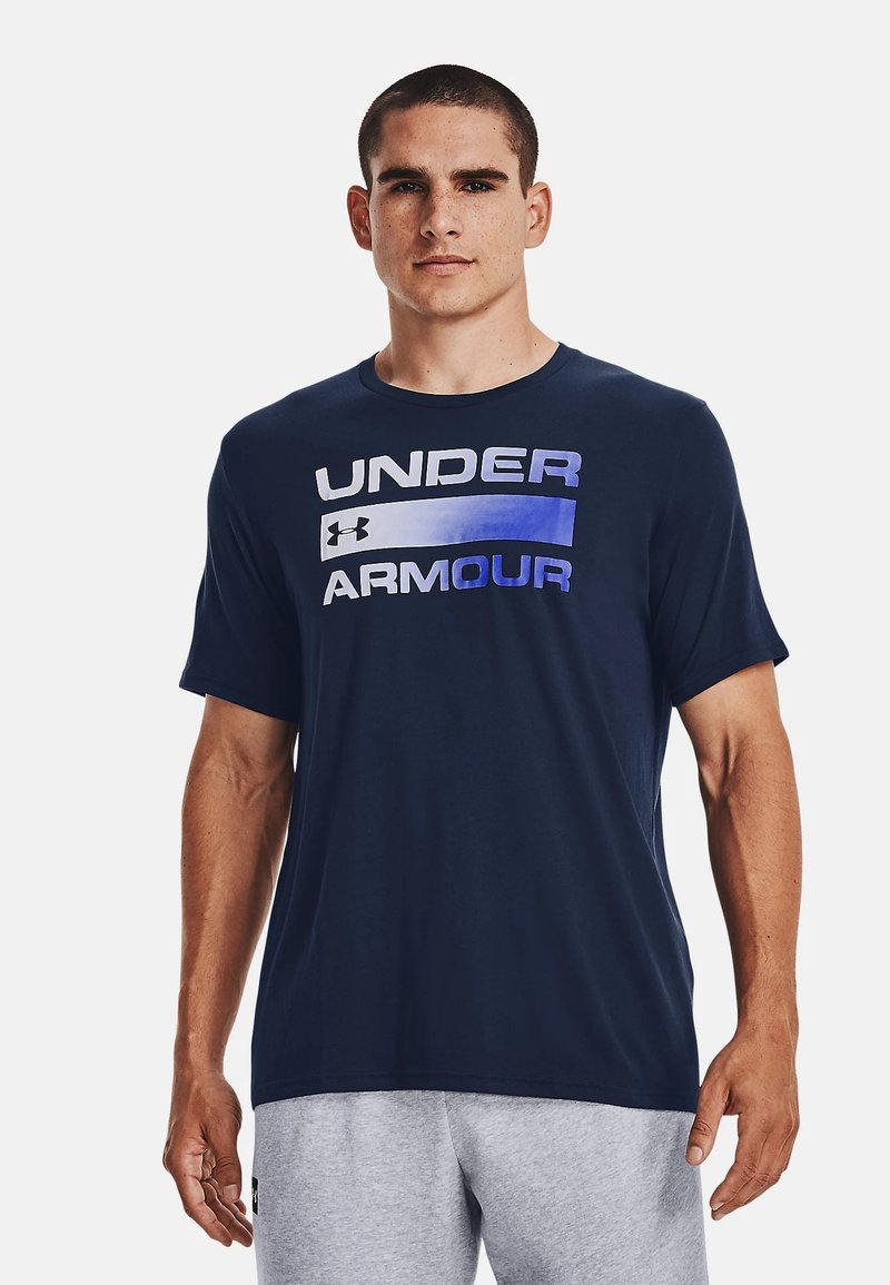 Mørkeblå kortermet t-skjorte laget av mykt stoff med "UNDER ARMOUR"-logoen i gradient hvit og blå over brystet. Enkel design.