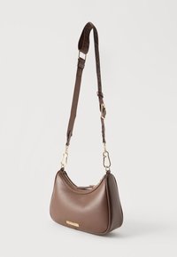 Καφέ δερμάτινη τσάντα ώμου με χρυσούς μεταλλικούς εξαρτήματα, ρυθμιζόμενο φαρδύ λουράκι, φερμουάρ κλεισίματος και διακριτική πλακέτα με λογότυπο στο μπροστινό μέρος.