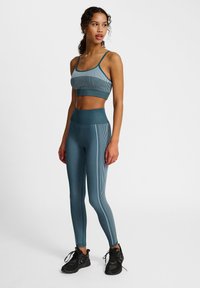 Turkusowy sportowy top z krótkim rękawem i legginsy z wysokim stanem w pionowe paski. Wykonane z elastycznego materiału, zestawione z czarnymi butami sportowymi.