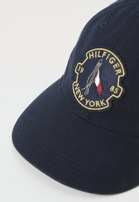 Casquette de baseball en coton bleu marine avec un logo brodé aux accents dorés, comprenant "HILFIGER," "NEW YORK," et un graphique coloré.