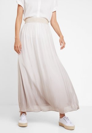 Jupe maxi beige clair en tissu fluide, avec une taille smockée et une texture douce et légère. Associée à des espadrilles blanches.