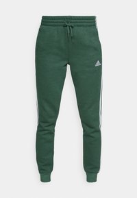 Gröna joggingsbyxor av mjukt material, med dragsko i midjan, smalnande ben, vita sidostråk och en broderad logotyp på framsidan.