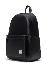 Mochila negra con una textura lisa, compartimento principal con cremallera, bolsillo frontal y una etiqueta de marca. Presenta un asa en la parte superior.